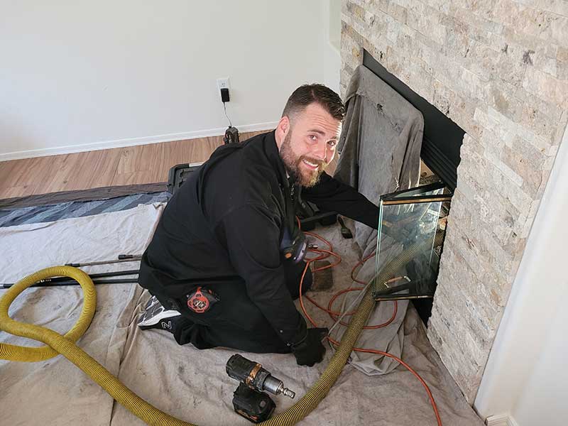 Guy cleaning chimney short hair with mustache and beard.  Floor covered with tarp as well and firebox.  Beautiful chimney brick.