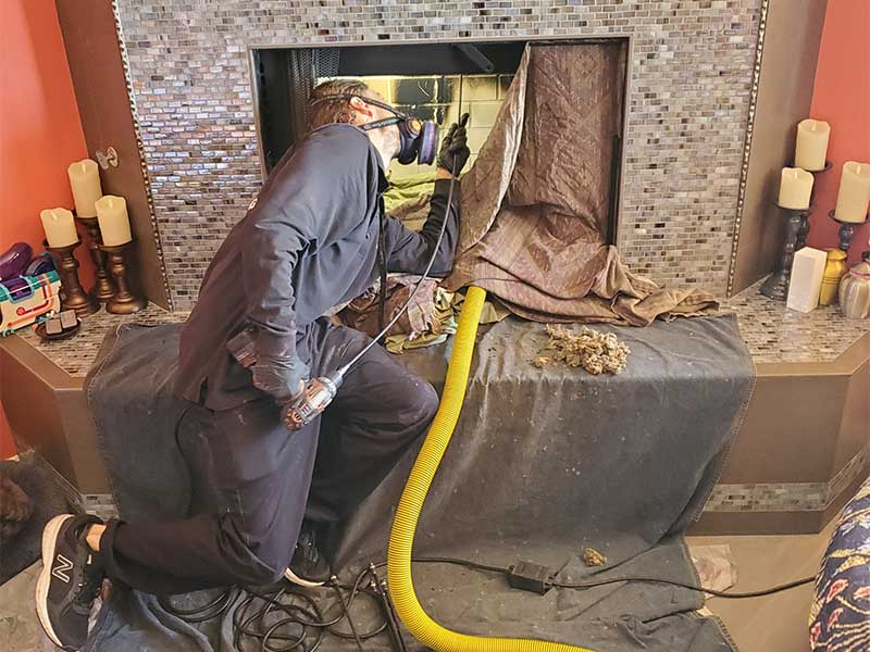 Tech cleaning firebox with yellow hose, tarp on the floor and candles on each side of the hearth.